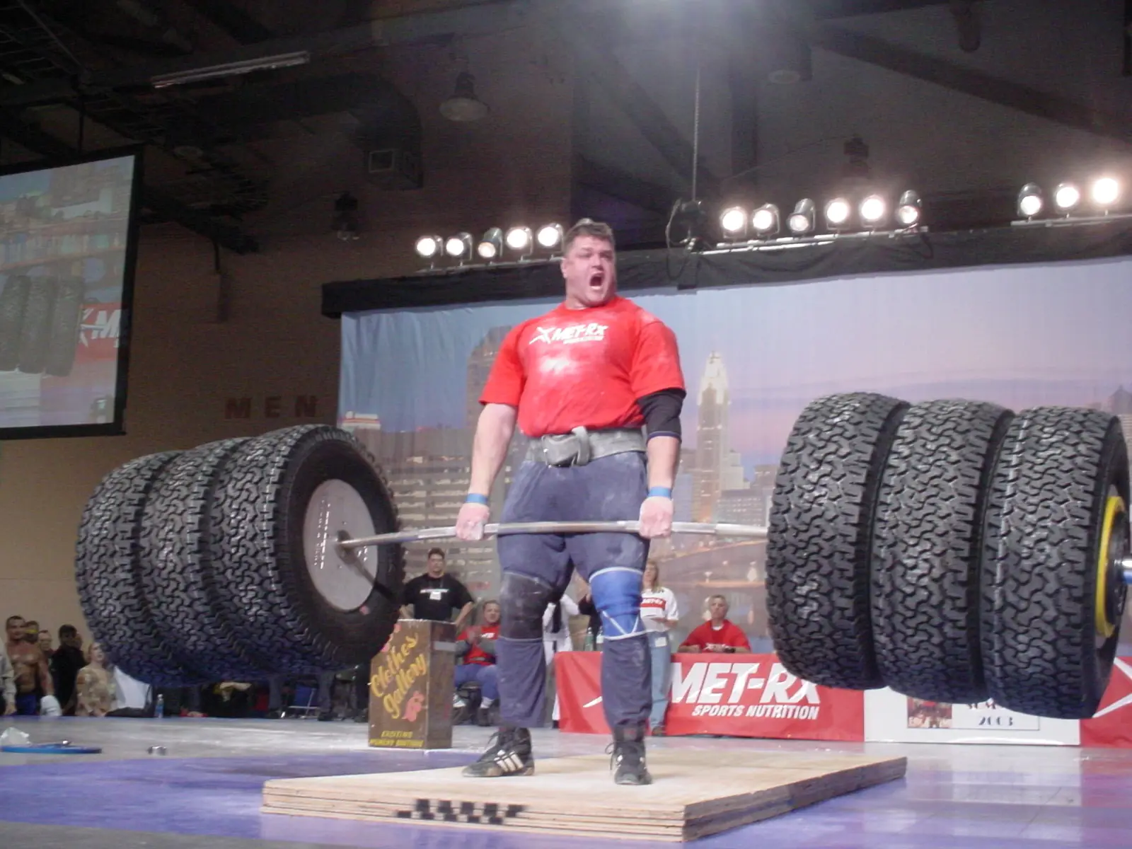 Brad Gillingham demonstrating incredible strength by deadlifting six hummer tires on a specially designed Olympic bar during a strongman competition.