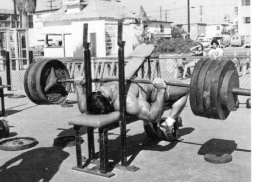 Bodybuilding champion Franco Columbu bench pressing a heavy barbell with ease at Muscle Beach, Venice, California
