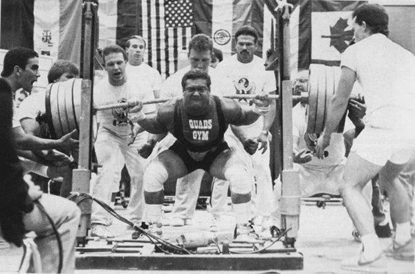 Ed Coan squatting heavy under a loaded barbell in competition