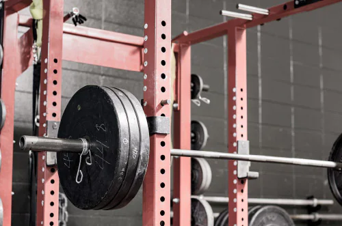 Main image shows a squat rack and Olympic barbell set prepared for an intense squat workout in a minimalist training environment.