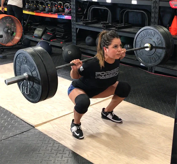 IRON COMPANY and Crossfit athlete Jackie Perez back barbell squatting with rubber bumper plates, Olympic weightlifting bar on top of a weightlifting platform.