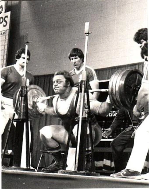 Powerlifter performing a heavy barbell squat with spotters