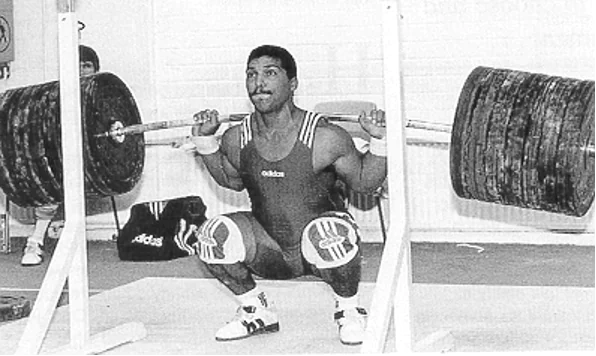 Olympic weightlifter performing a deep raw back squat.